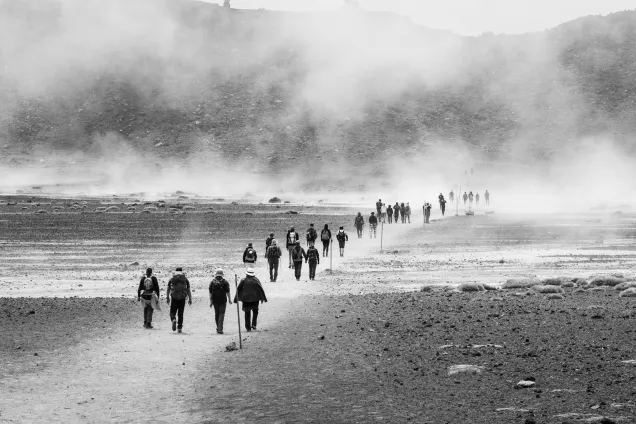 People moving in a line into a dusty desert. Photo.