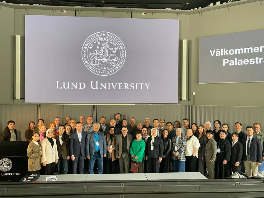 A group of people is gathered in front of a large screen displaying the Lund University logo and text. They stand closely together, smiling warmly.